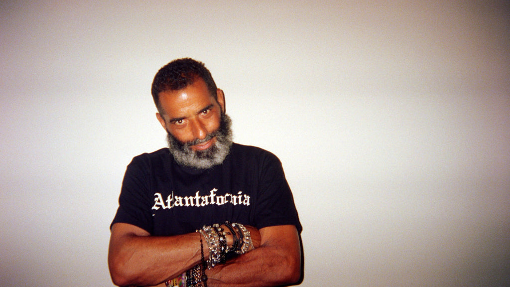 Man wearing a black t-shirt with 'Atlantafornia' text, leaning against a white wall